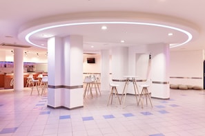 A modern hotel lobby with a circular seating area, white pillars, and a check-in counter in the background. - Hotel Caribe Youth Hotel (Lloret de Mar)