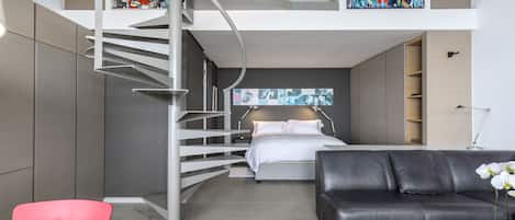 A modern interior with a staircase leading to a loft bedroom, a black leather sofa, and a small table.