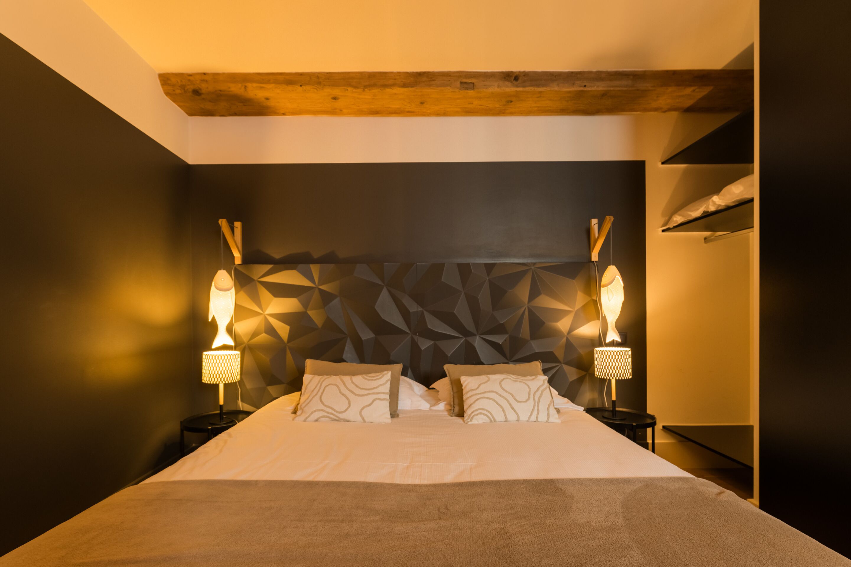 Una cama bien hecha con un cabecero de estampado geométrico, dos lámparas de noche y una viga de techo de madera.