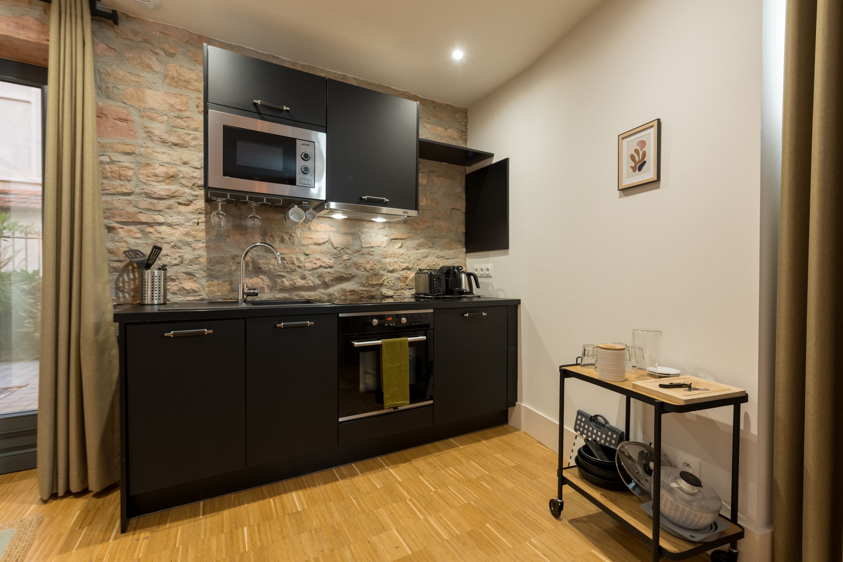 Cozinha moderna com painel de pedra, armários pretos, forno embutido e uma pequena mesa com utensílios de cozinha.
