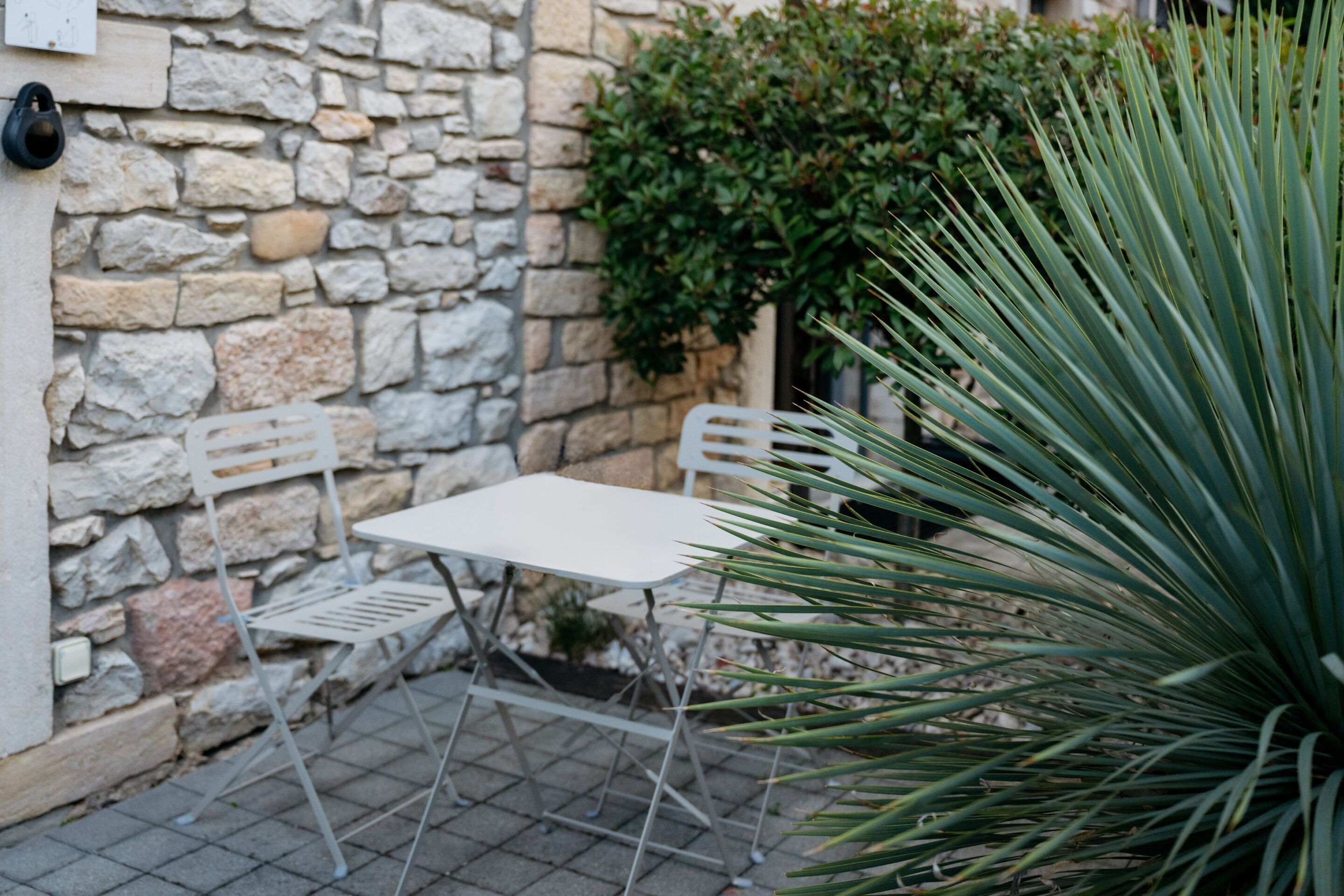 Una pequeña zona de estar al aire libre con un muro de piedra, una mesa blanca y una silla.