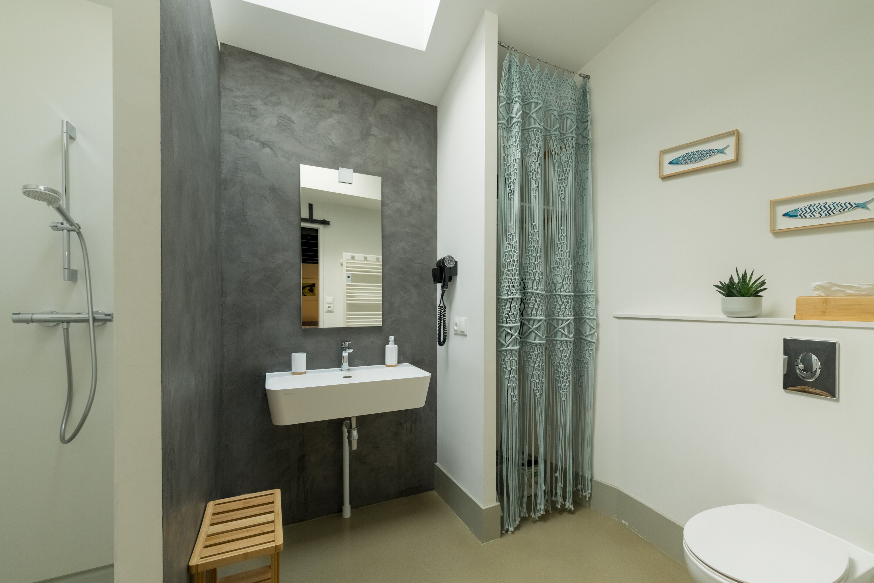 A modern bathroom with a grey accent wall, a white sink, a shower, and a toilet.