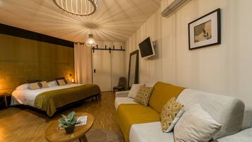 Ein Hotelzimmer mit Bett, Sofa, einem kleinen Tisch mit Pflanze, einem an der Wand montierten Fernseher und einer Deckenleuchte.