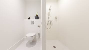 A modern bathroom with a toilet, a shower, and a small shelf with plants.