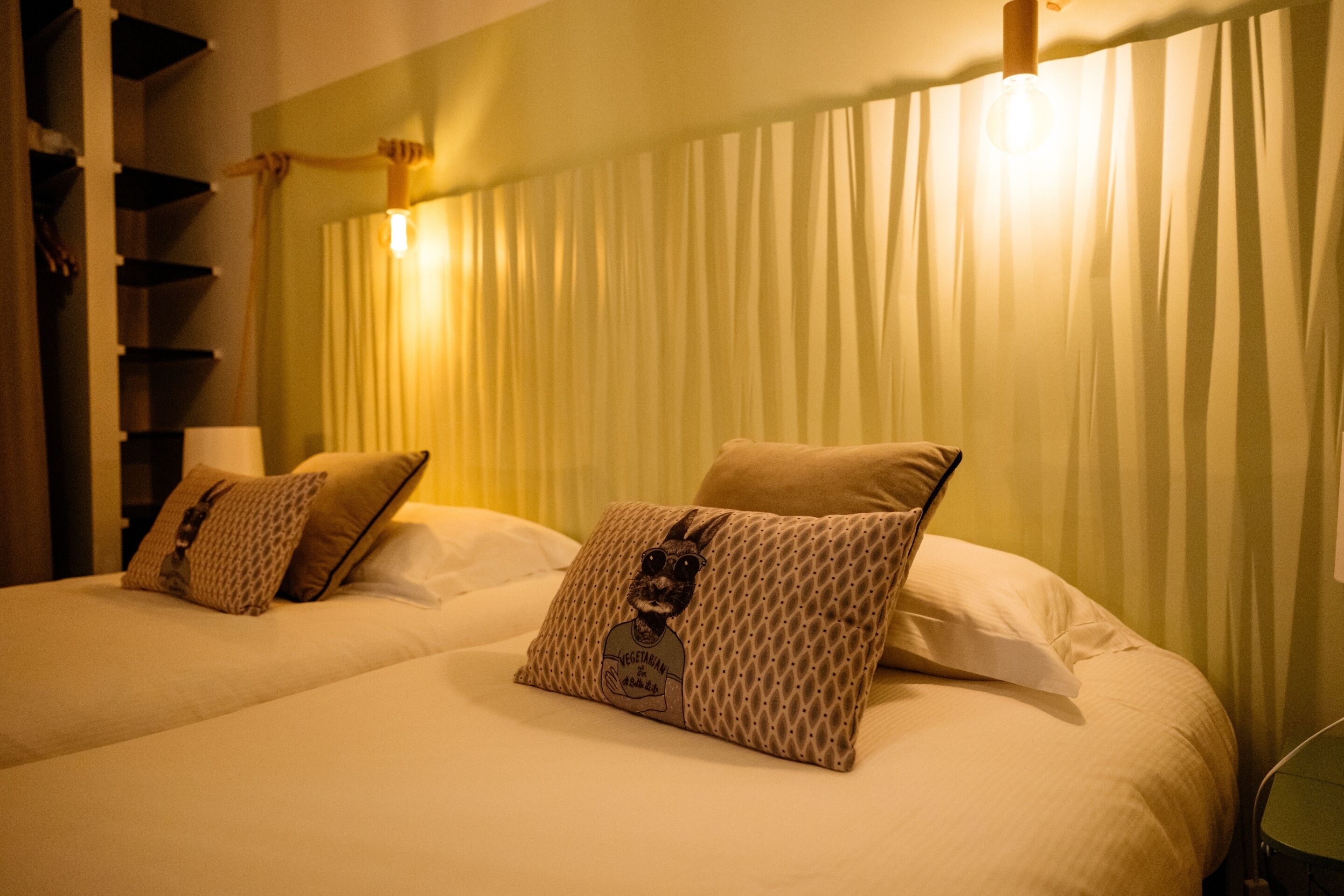 A hotel room with two beds, each with a patterned pillow and a lamp on the nightstand.