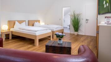 A hotel room with a bed, bedside tables, a TV, a potted plant, and a wooden floor.