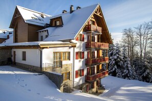 A multi-story chalet with a steep roof, wooden balconies, and a stone foundation. - Luxury Apartments Bolf (Maribor)