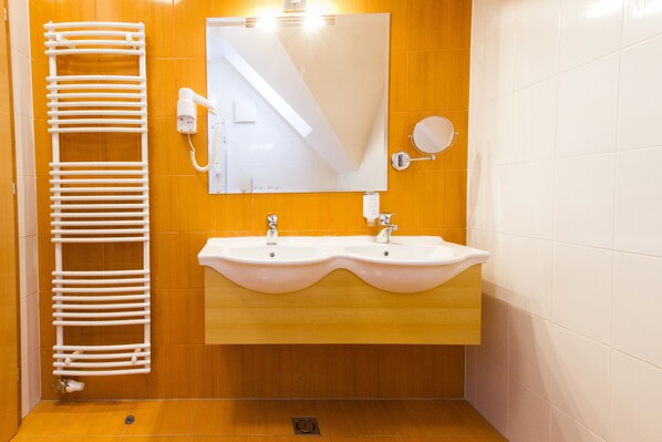 A bathroom with a wooden vanity, two sinks, a towel rack, a mirror, and a wall-mounted light fixture. - Luxury Apartments Bolf (Maribor)