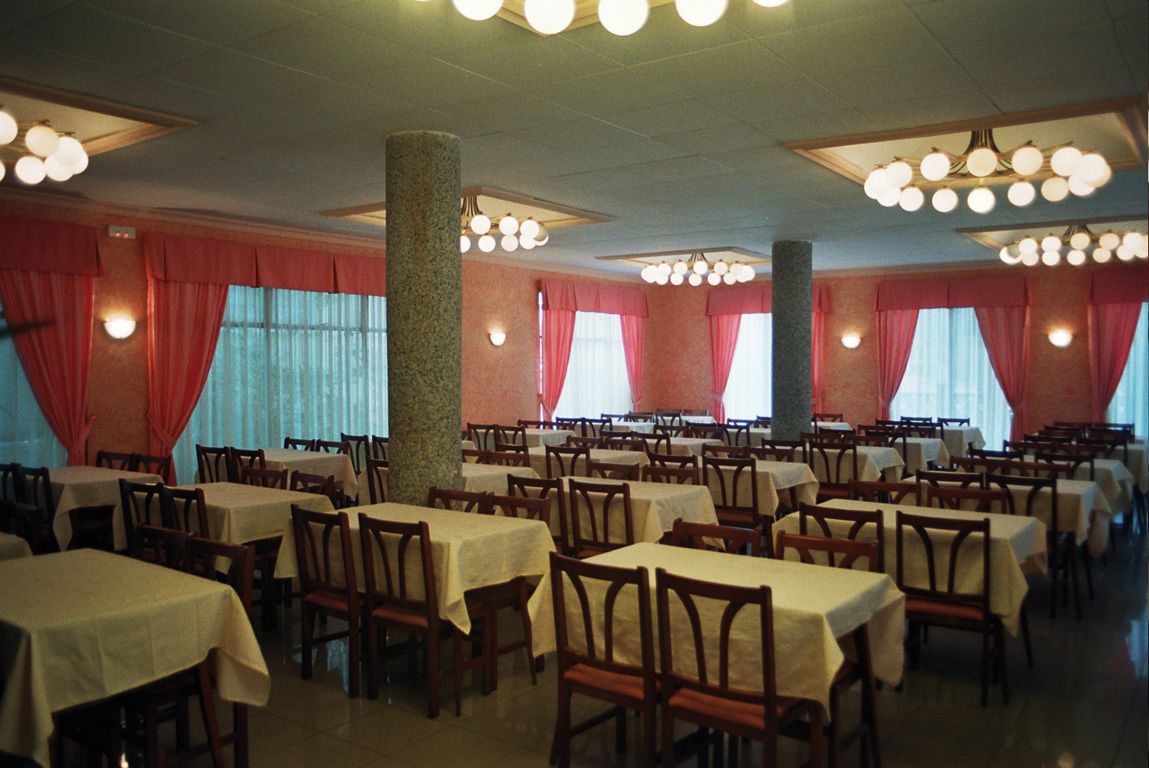 Un amplio comedor con varias mesas y sillas, cortinas rojas y un pilar central.