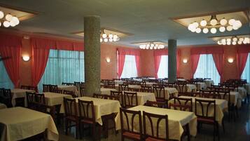 Un amplio comedor con varias mesas y sillas, cortinas rojas y un pilar central.