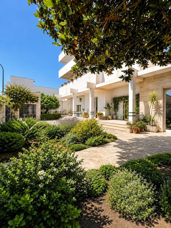 A modern building with a courtyard, surrounded by various plants and shrubs. - Canneddi Boutique Farm (Avetrana)
