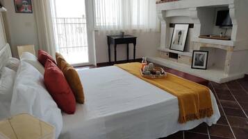 A hotel room with a bed, a small table, a chair, a fireplace, and a balcony.