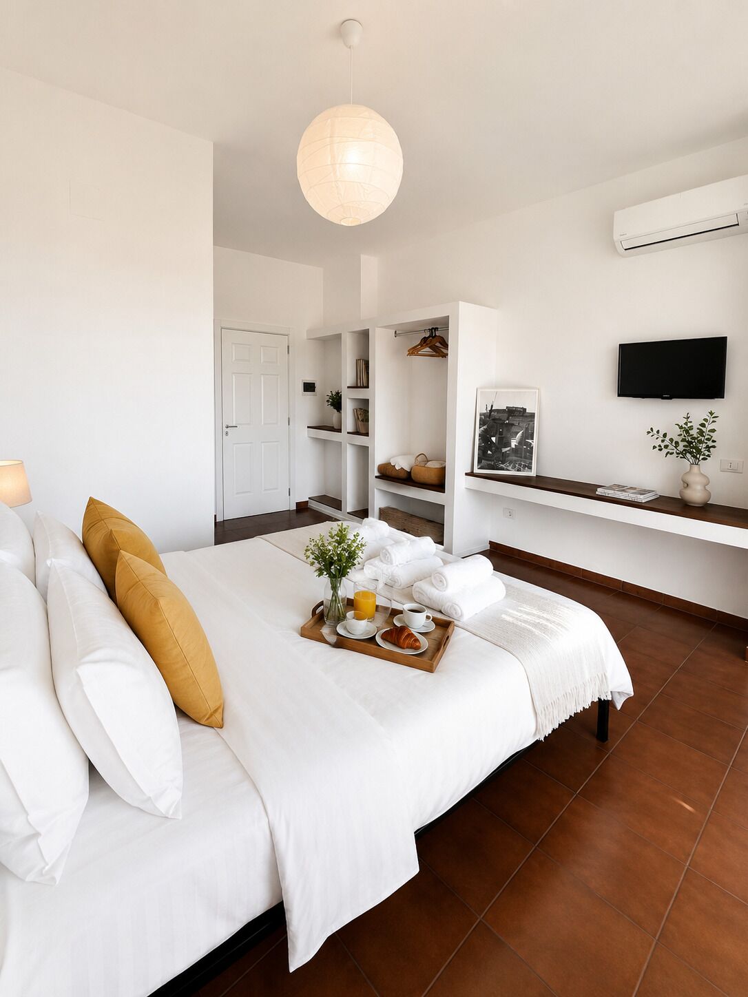 A hotel room with a bed, a bedside table with a tray of breakfast, a TV, and a wall-mounted air conditioner.