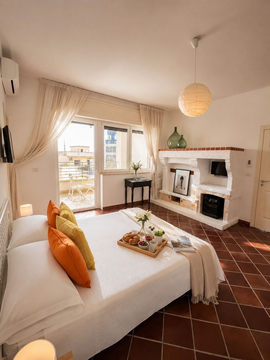 A hotel room with a bed, a fireplace, a dining table with breakfast, and a balcony with curtains.