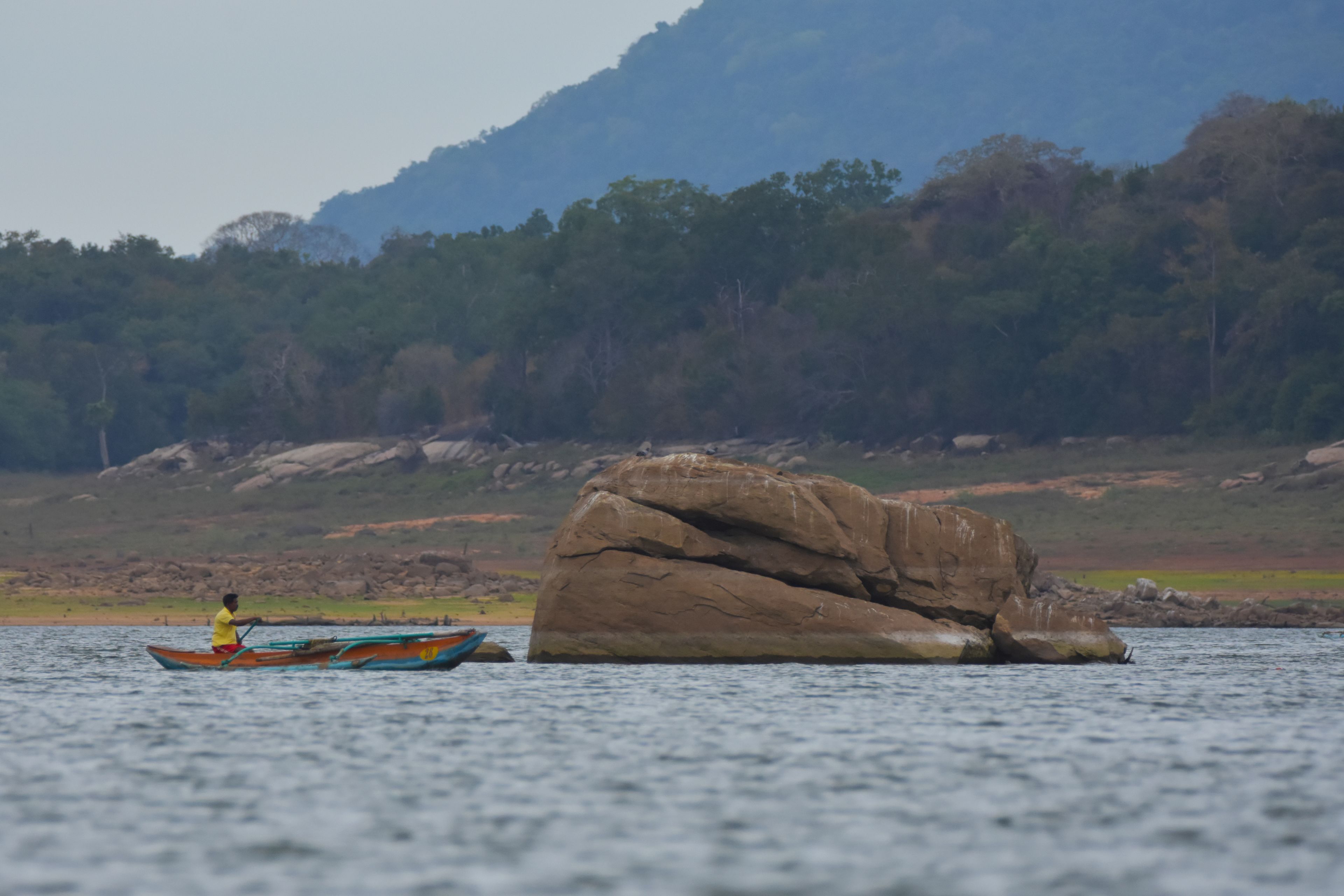 A person in a boat on a calm body of water with a large rock formation in the background.
