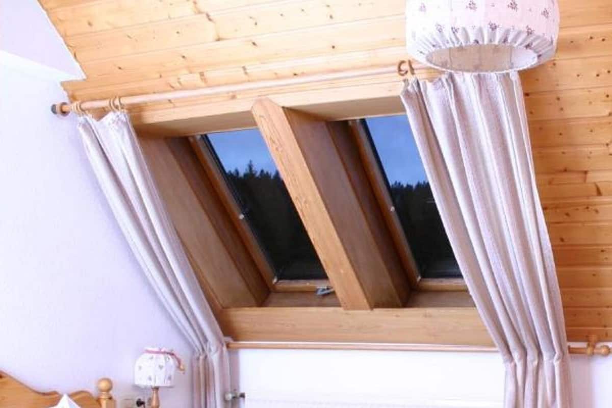 Un dormitorio con techo de madera, tragaluz, cama y mesita de noche con lámpara.