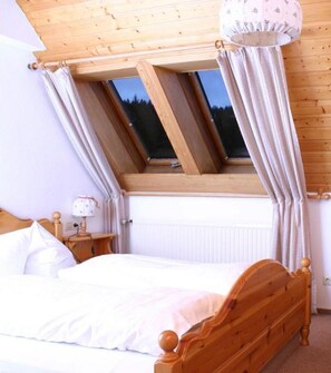Un dormitorio con techo de madera, tragaluz, cama y mesita de noche con lámpara.
