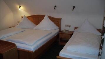 Una habitación con dos camas de madera, cada una con cabecero de madera y ropa de cama blanca. Hay mesitas de noche y una lámpara fijada a la pared.