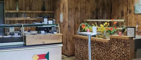 A restaurant interior with a wooden wall, a tiled floor, a counter with a vase of flowers, and a metal stool.