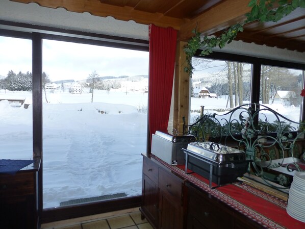 A room with a large window overlooking a snowy landscape, a wooden cabinet, and a metal decorative piece. - Gasthaus Backhof-Helmle (Breitnau)