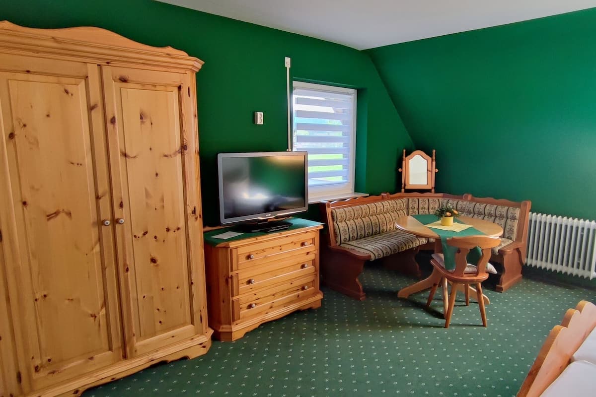 Una habitación con pared verde, armario de madera, televisor, banca y cama.