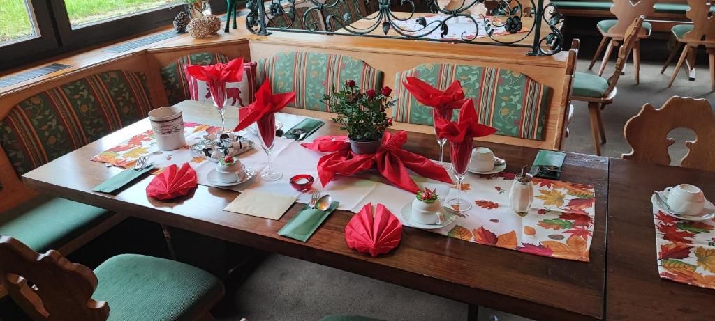 Una mesa de comedor con servilletas rojas, una pequeña planta en maceta y un mantel con estampado floral.