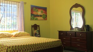 A bedroom with a bed, a dresser, a mirror, and a painting on the wall.