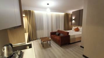 A hotel room with a bed, a sofa, a small table, a kettle, and a tray with cups and a teapot.