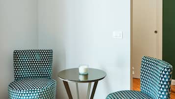 Habitación de esquina con dos sillones estampados, una mesita redonda y una puerta blanca.