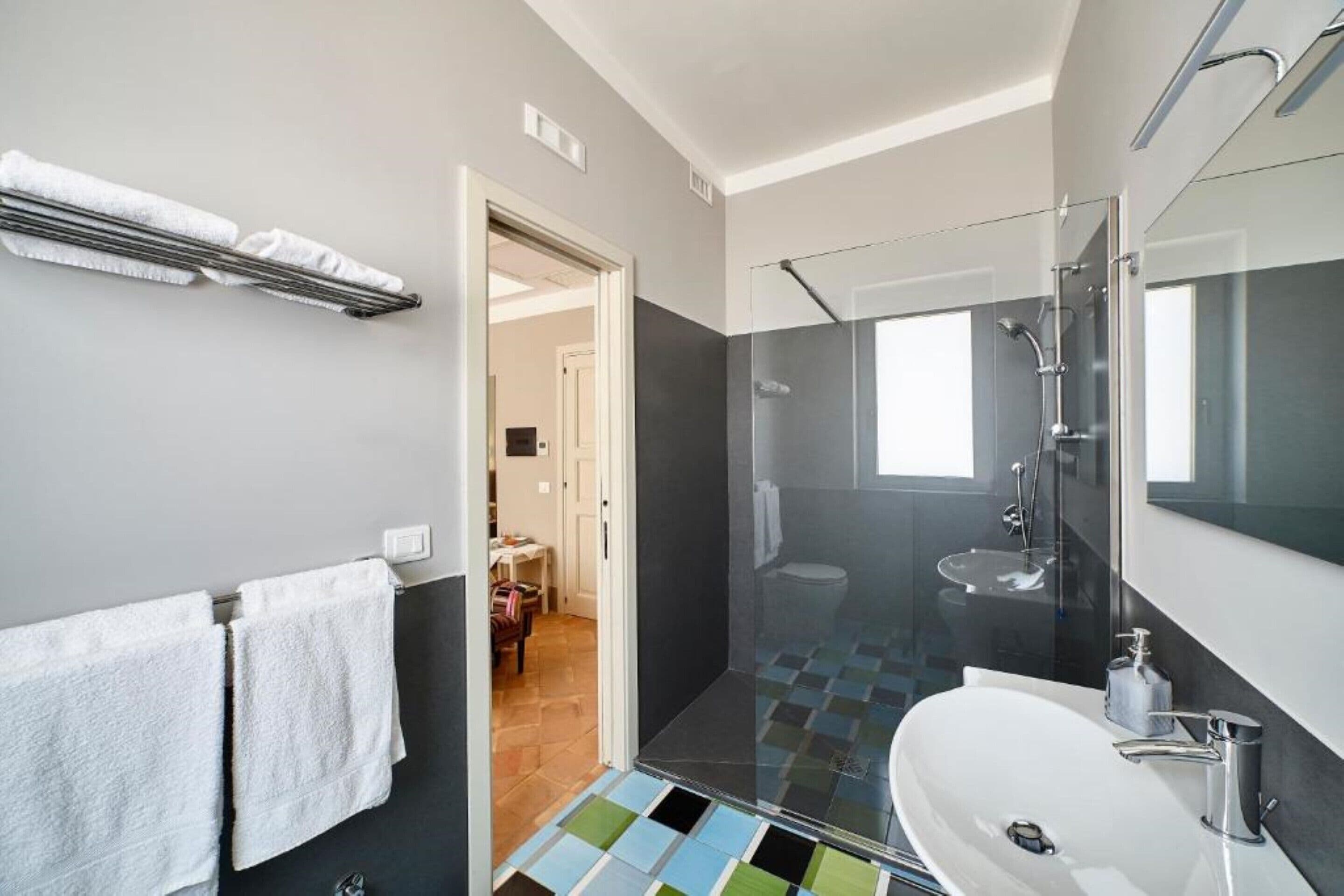 Une salle de bain moderne avec une douche à parois de verre, un lavabo blanc et un sol carrelé.