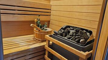 A sauna room with wooden slats, a bench, a bucket with a plant, and a container of rocks.