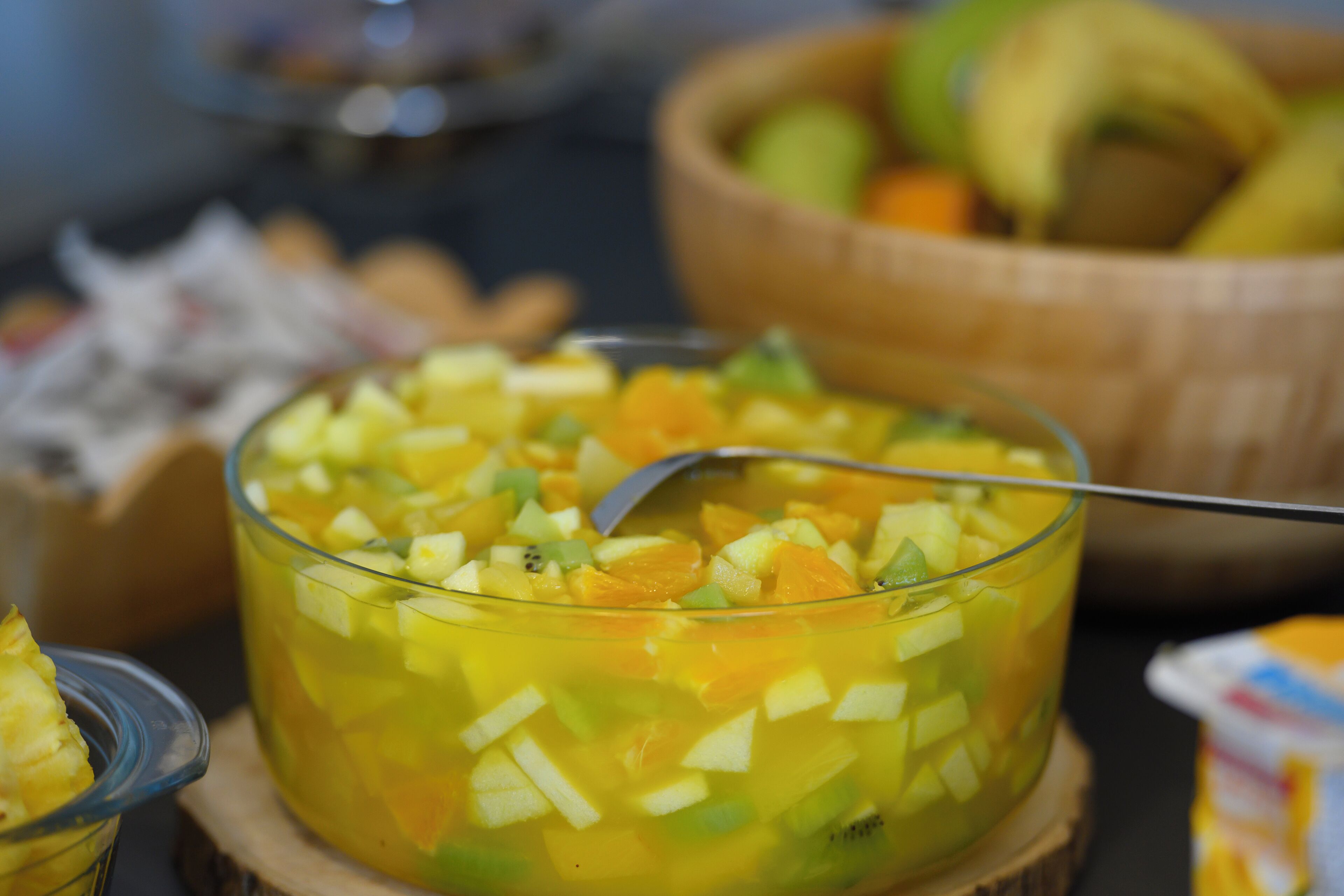 Un cuenco de vidrio lleno de fruta picada, un tazón de madera con más fruta y una cuchara en primer plano.