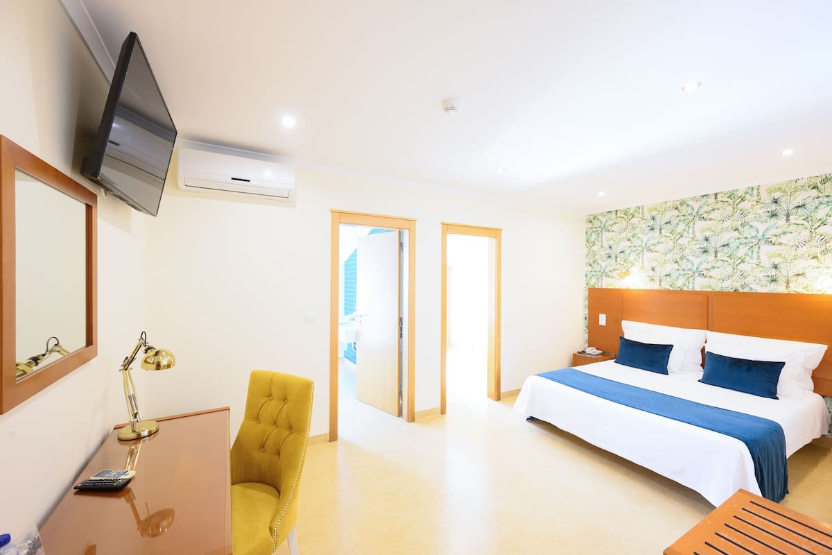 A hotel room with a bed, a desk with a lamp, a chair, and a TV mounted on the wall.