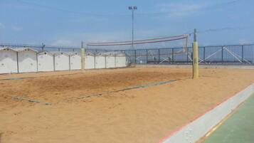 A sandy volleyball court with a net, surrounded by a fence and covered buildings.
