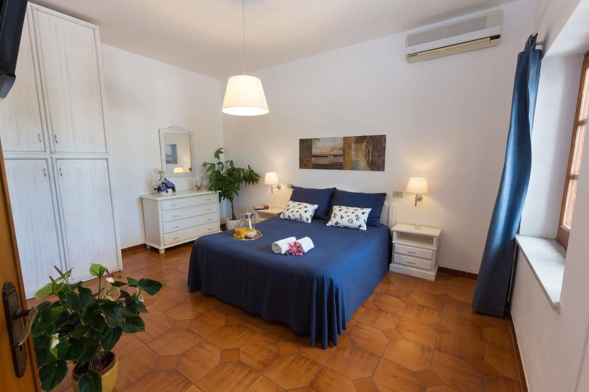 A bedroom with a bed, bedside tables, a dresser, a potted plant, and an air conditioning unit.