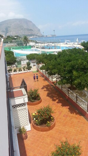 A rooftop terrace with two people walking, a pool area, and a mountainous backdrop. - La Marsa Vacances (Palermo)