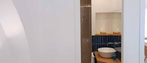 Een moderne badkamer met een grote witte wastafel, een douchegedeelte betegeld met blauwe tegels en een houten wastafelmeubel.