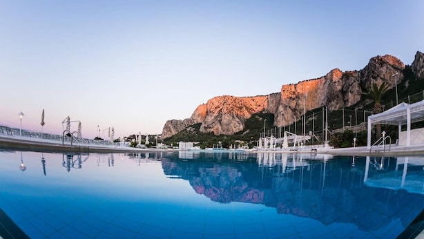 A swimming pool with clear blue water, a white gazebo, and a rocky mountain in the background. - La Marsa Vacances (Palermo)