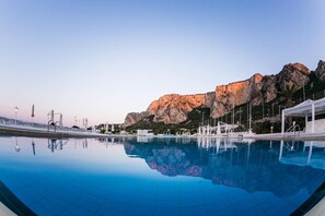Une piscine à l’eau d’un bleu cristallin, un belvédère blanc et, au loin, une montagne rocheuse.