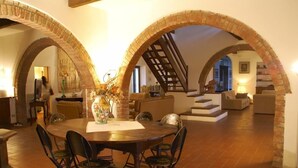 A spacious loft with a high ceiling, exposed brick arches, a central dining table with chairs, and a staircase leading to an upper level.