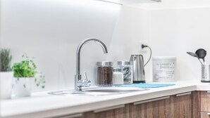 Moderni keittiö, jossa on ruostumattomasta teräksestä valmistettu pesuallas, sininen alusta ja erilaisia keittiötarvikkeita työtasolla.