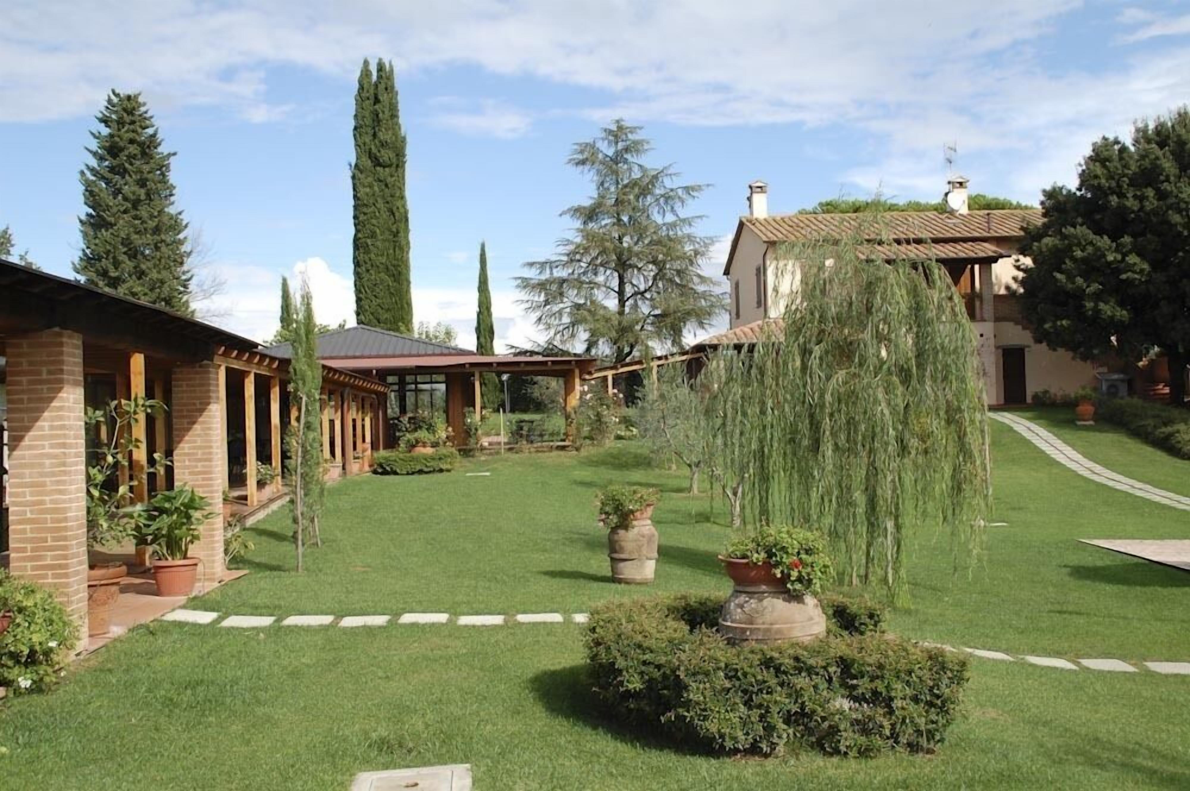 Um jardim bem cuidado com um edifício de tijolos, uma pérgula e diversas plantas.
