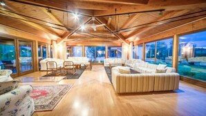 Un vaste salon doté d’un plafond en bois, de grandes fenêtres et d’une vue sur la piscine.