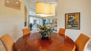 A dining area with a round table, orange chairs, a hanging light fixture, and a painting on the wall. - 170 Post Court- Beautiful Bay View in this Lovely 3 bedroom home! (Marco Island)