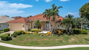 A single-story house with a red-tiled roof, a front door, and a small front yard with palm trees and shrubs. - 170 Post Court- Beautiful Bay View in this Lovely 3 bedroom home! (Marco Island)