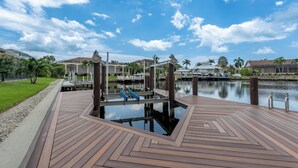 Una terraza de madera con un elemento acuático, un muelle y casas al fondo.