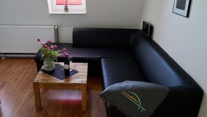 A living room with a wooden coffee table, a black sofa, a grey throw blanket, and a vase with flowers. - Strandleben Fehmarn - Ferienwohnung Nord (Fehmarn)