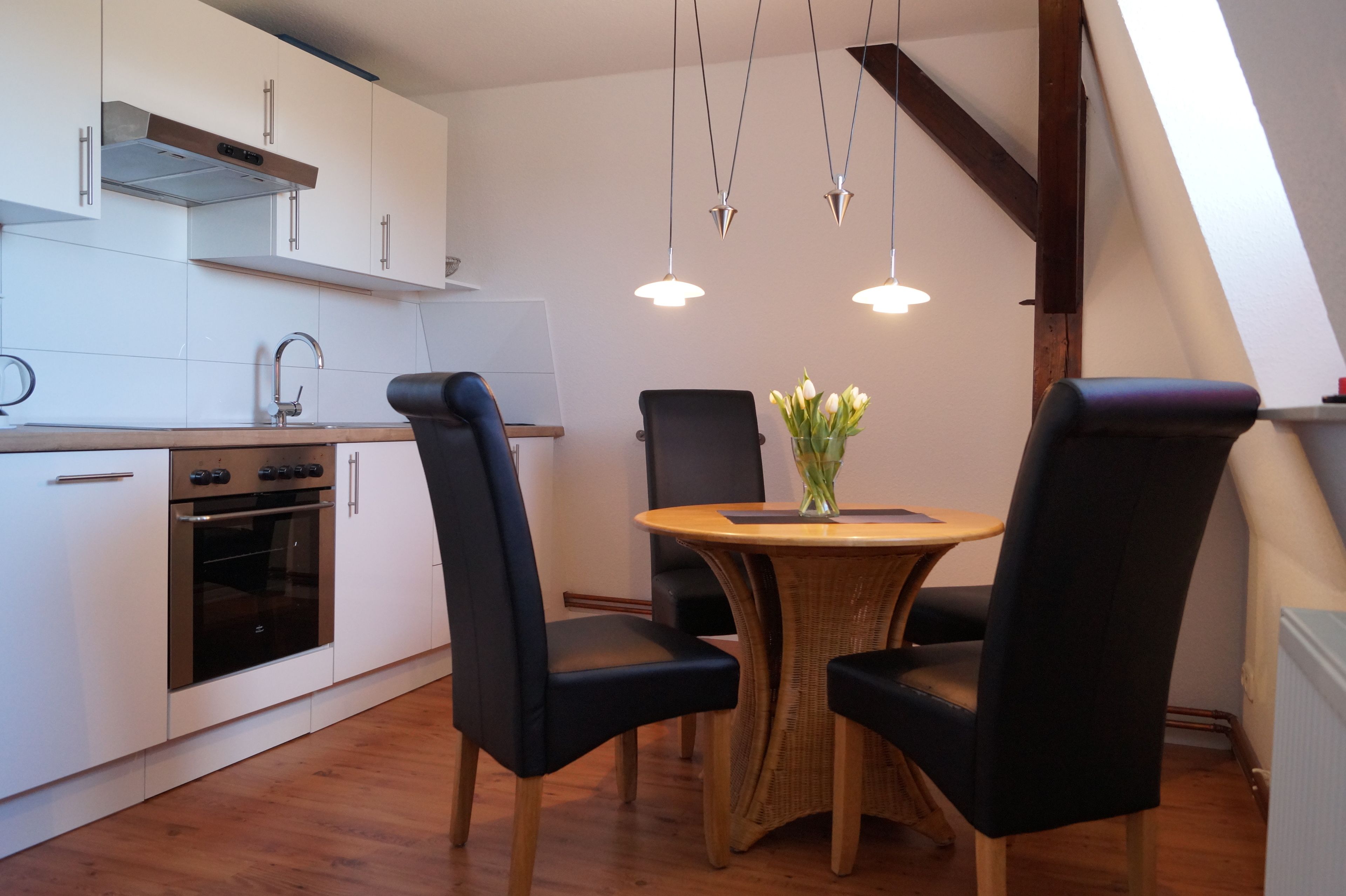 A modern kitchen with white cabinets, a built-in oven, and a dining area with a round table and four chairs.