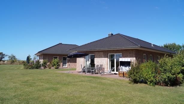 A two-story house with a brick exterior, a covered patio with outdoor furniture, and a clear blue sky. - Strandleben Fehmarn - Ferienwohnung Nord (Fehmarn)