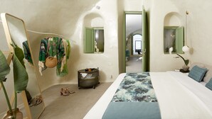 A bedroom with a bed, a mirror, a plant, and a small cart with items. - Gitsa Cliff Luxury Villa (Santorini)